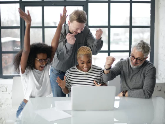 group of people stood around a laptop cheering